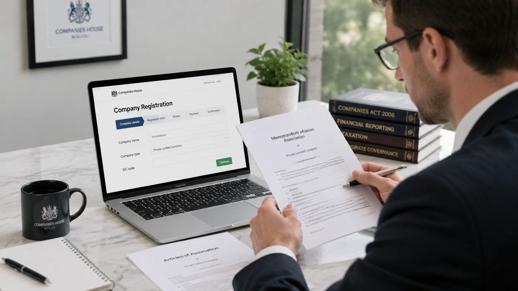 A professional man in a suit reviews company registration documents while using a laptop at his office desk.